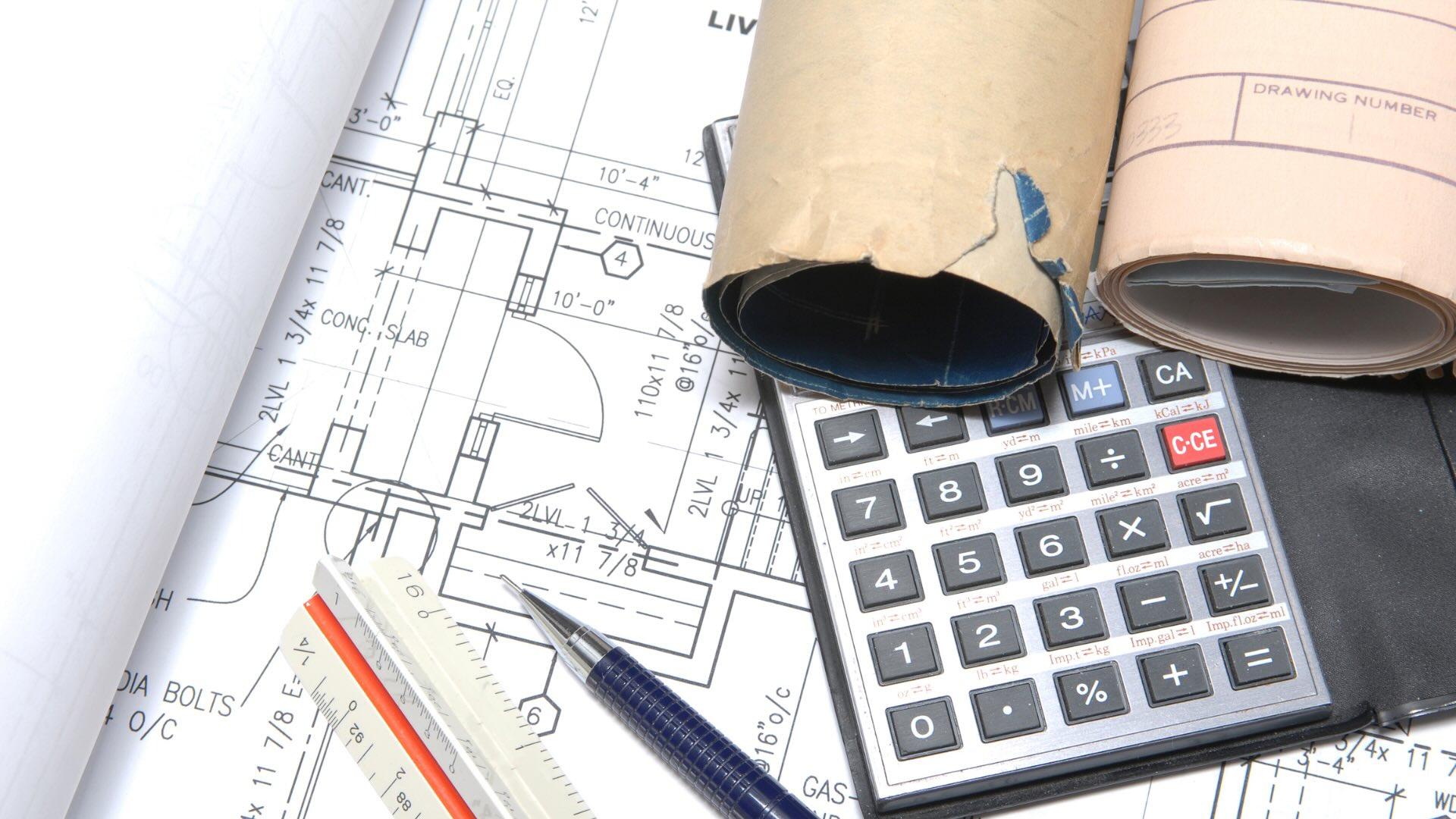 Architectural blueprints laid out on a desk with a calculator, ruler, and a mechanical pencil.